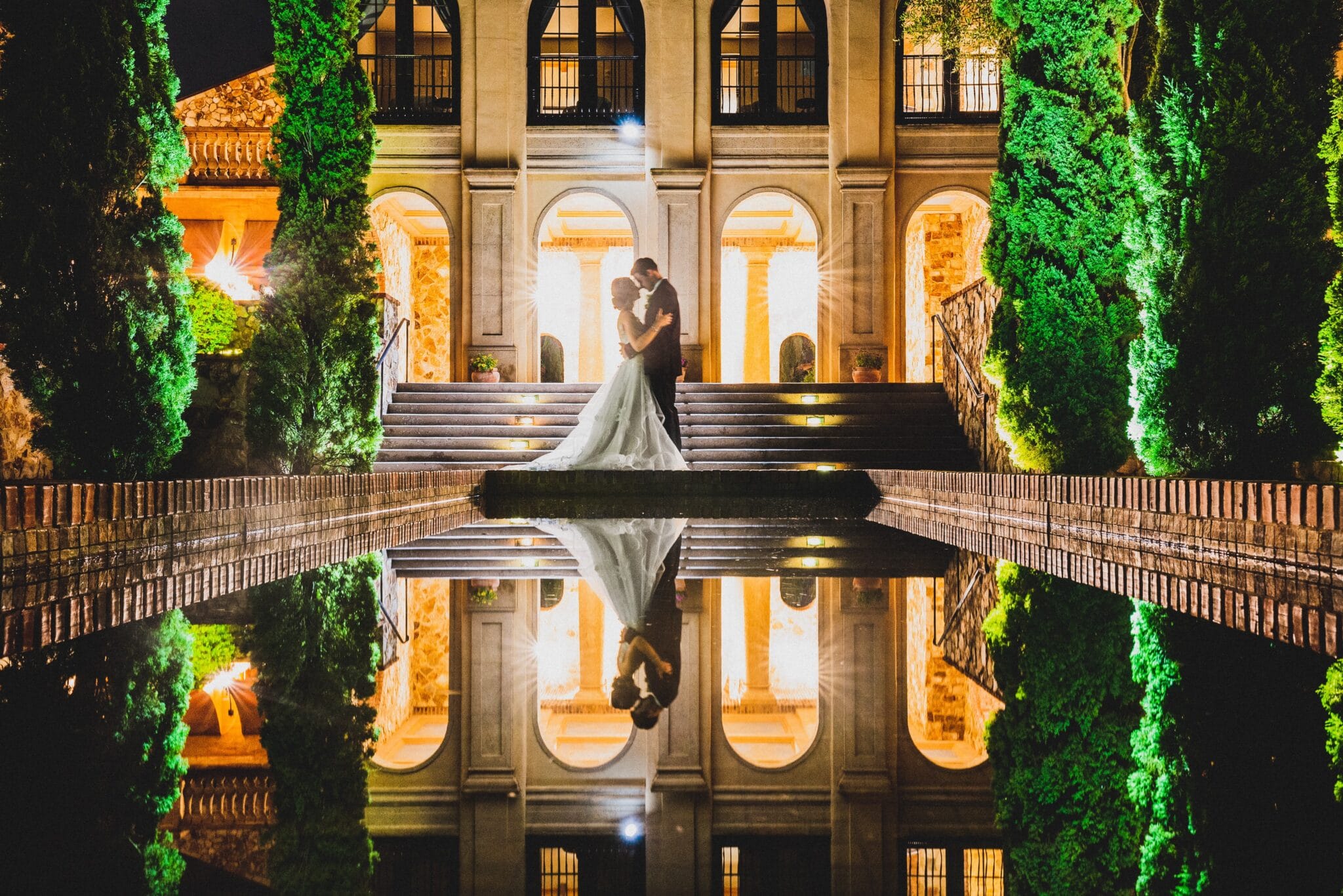 Bride and groom illuminated in water in front of building at night
