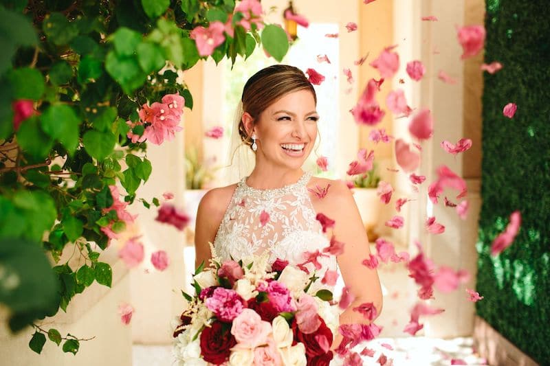 Just Marry bride laughing while holding bouquet and rose petals are thrown in the air around her
