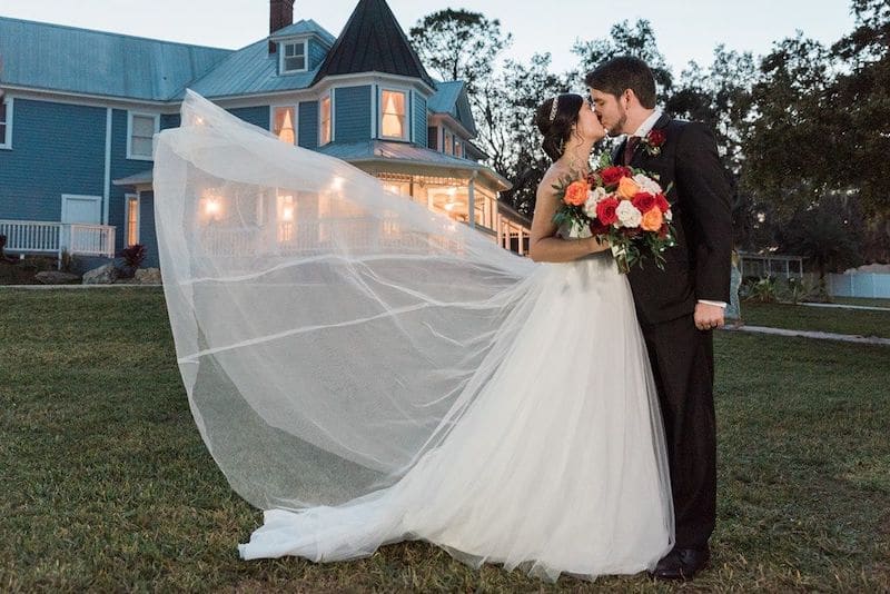 Just Marry bride and groom kissing outside with bride's train flowing in the breeze