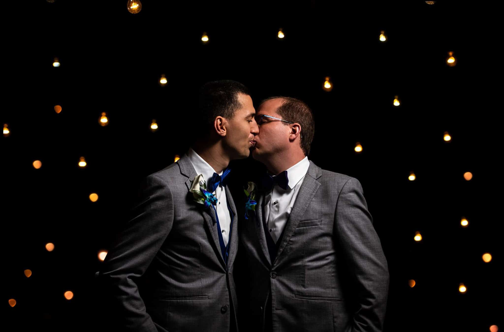 grooms kissing with lights in background