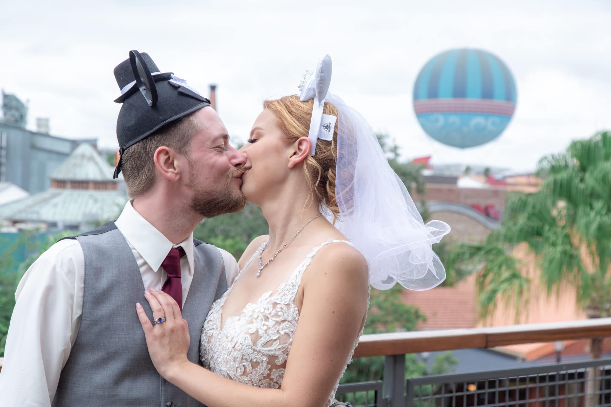 bride and groom kissing with mickey and minnie wedding ears in front of hot air balloon at disney springs florida