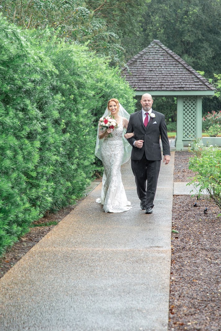 bride holding bouquet and fathers arm walking down the sidewalk to wedding ceremony