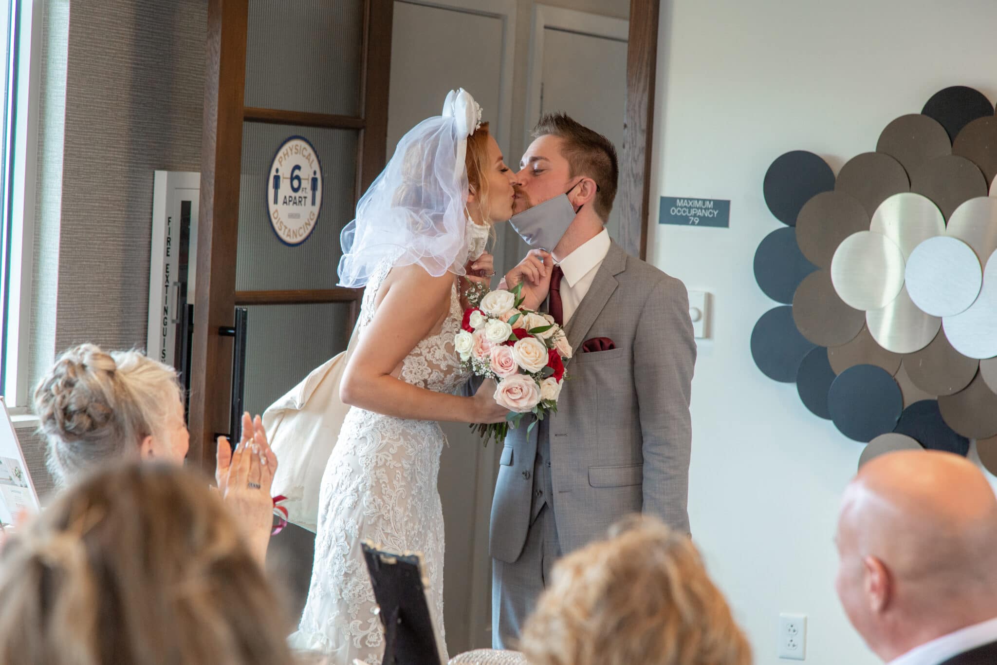 bride and groom remove masks once entering their wedding reception space to kiss while bride holds bouquet