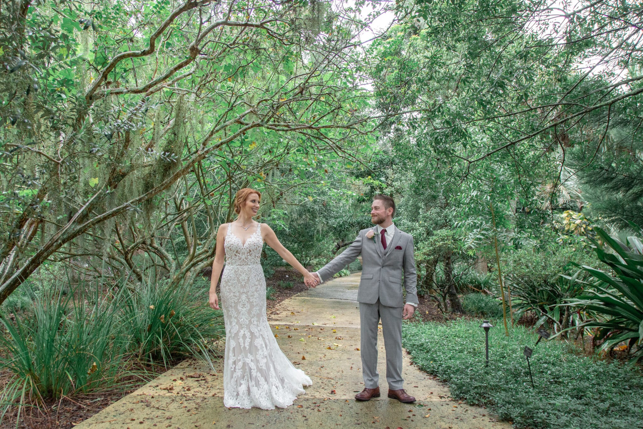 lush greenery and trees surrounding bride and groom holding hands on the sidewalk