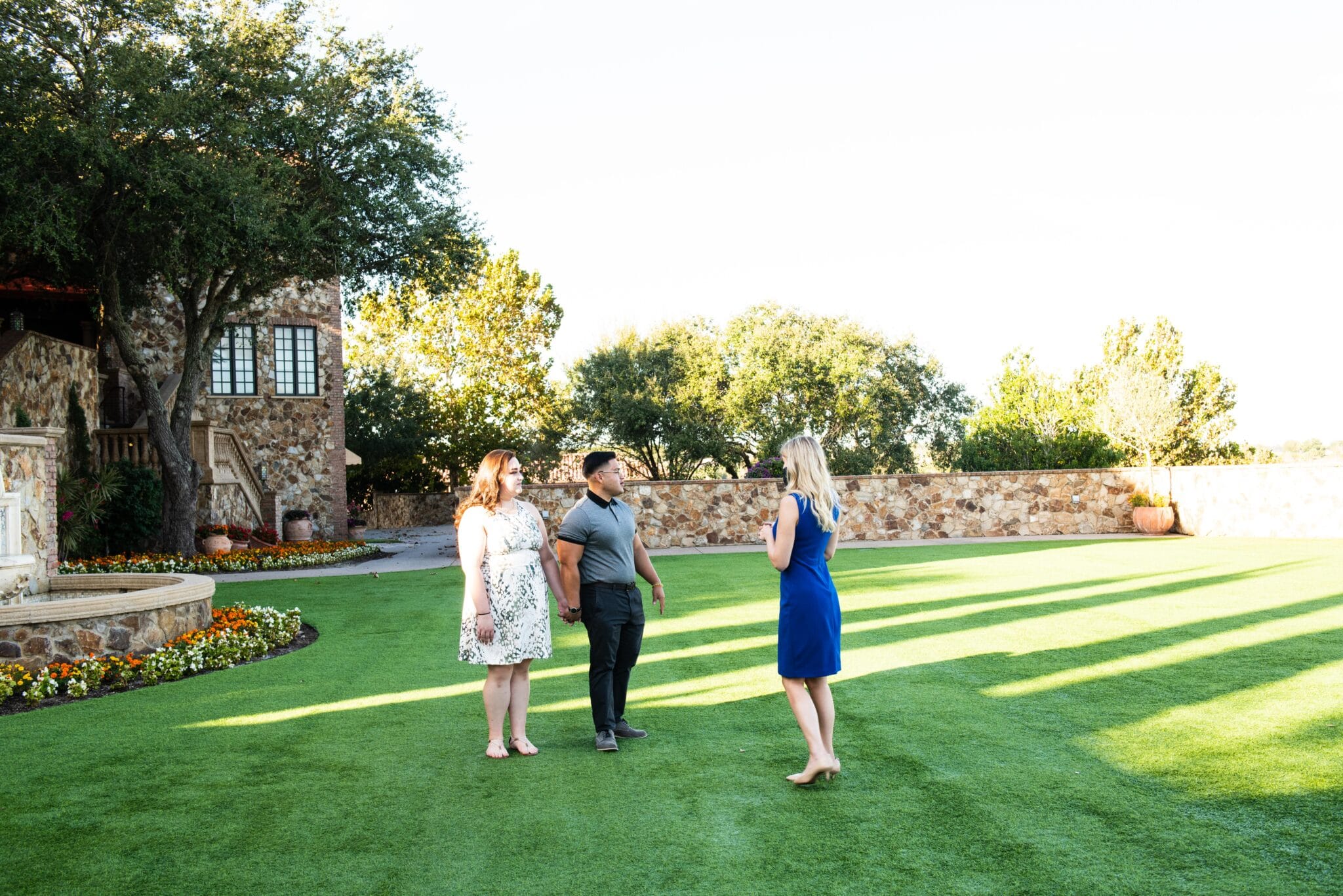 couple holds hands while listening to wedding venue coordinator speak about the property on the ceremony lawn at tuscan inspired venue