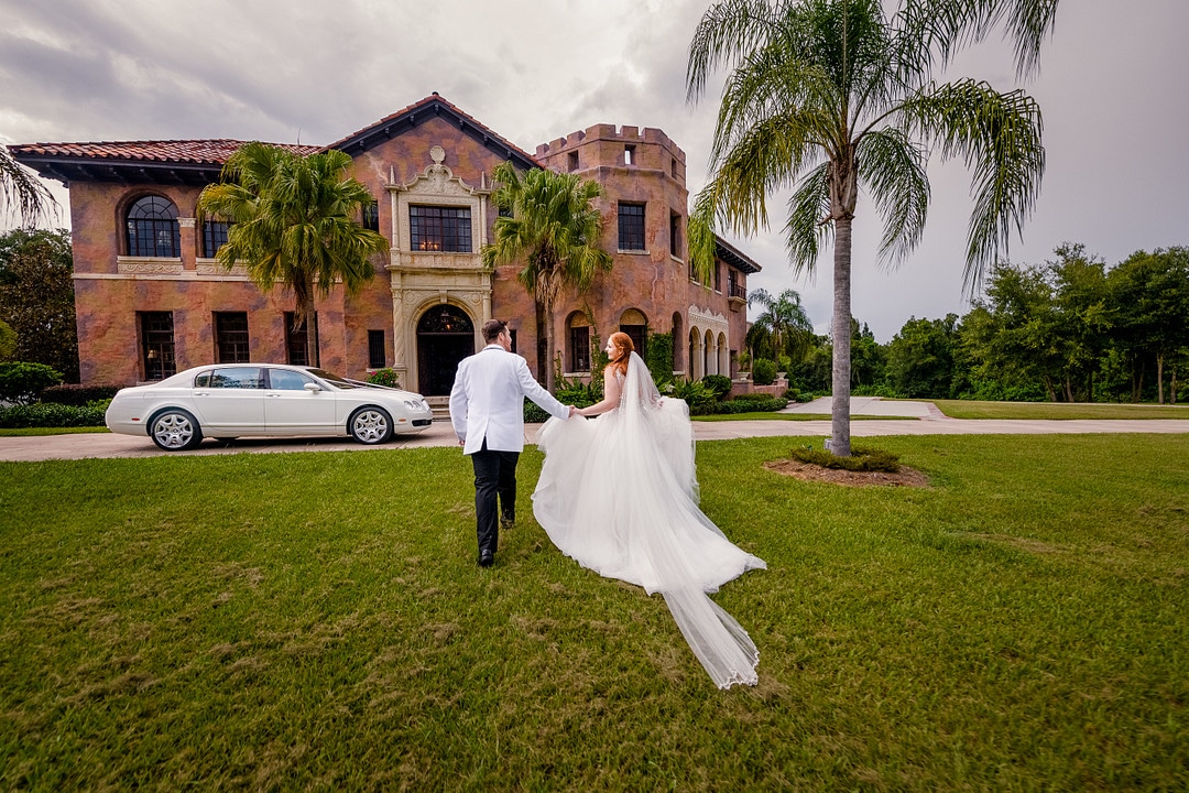 bride and groom walking towards castle wedding venue in FL with classic white wedding car parked in front