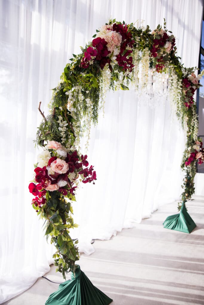 round arch covered in greenery and pink flowers in front of white curtain
