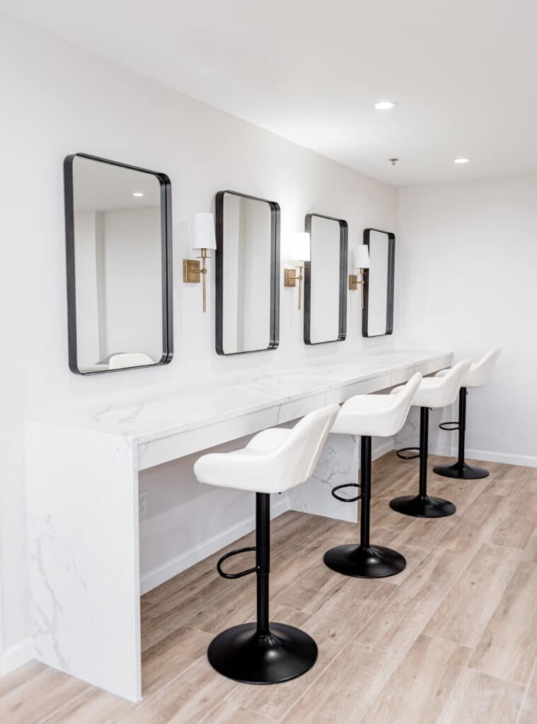 tall white stools in front of white counter with mirrors and lights