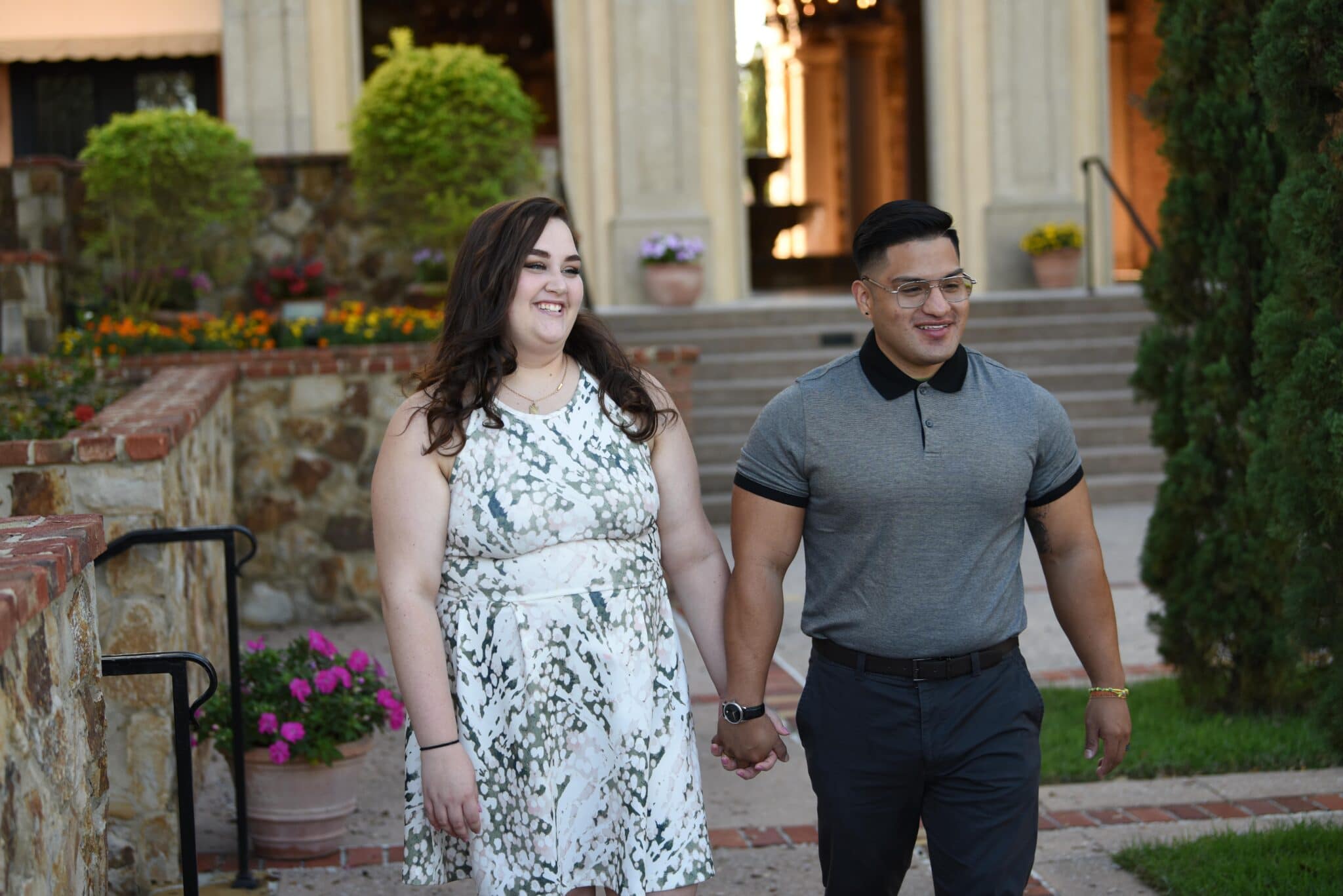 man in polo and dress pants holds hands with girl in dress at wedding venue while smiling