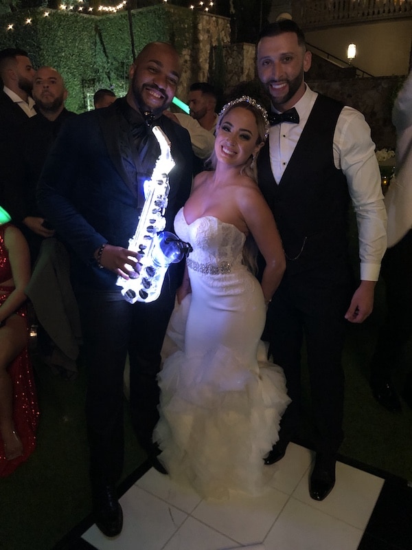 RLE3 Music with a lit up led saxophone stands next to a bride and groom on their wedding day