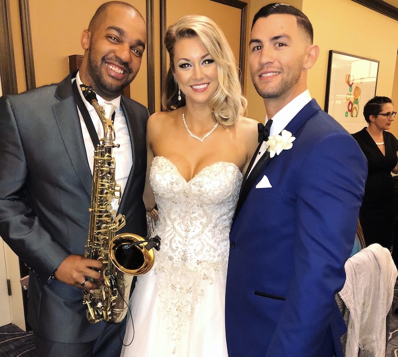 saxophone player poses next to a bride and groom after playing music at their wedding