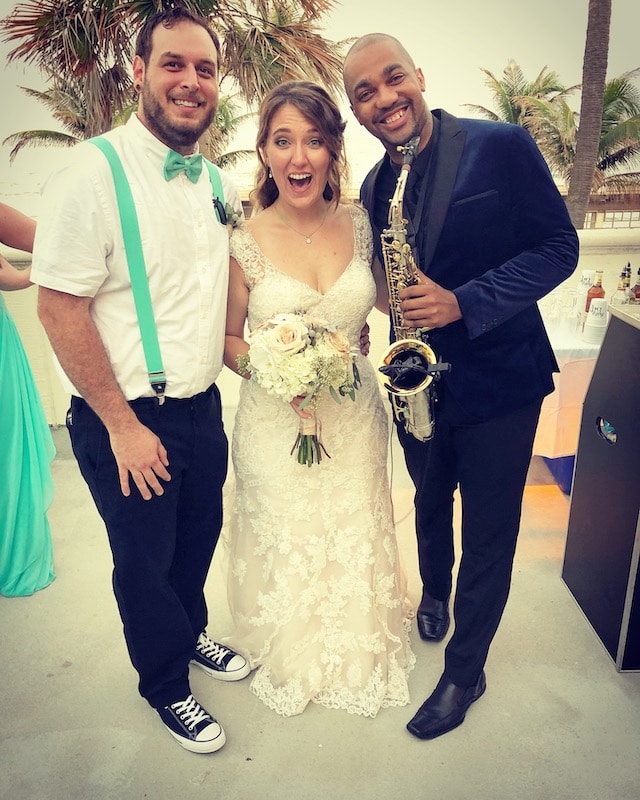 saxophone player posing with a bride and groom during their outdoor beach wedding