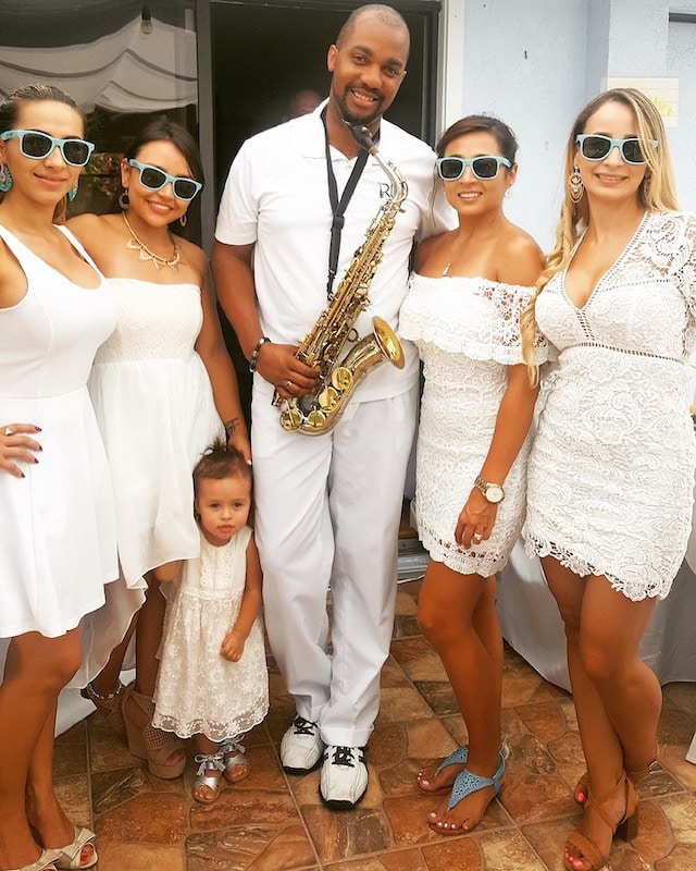 saxophone player wearing all white posing next to bridesmaids and flower girl