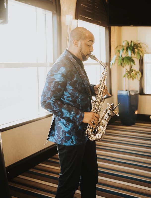 saxophone player in a blue and black tux coat performing at an indoor wedding ceremony