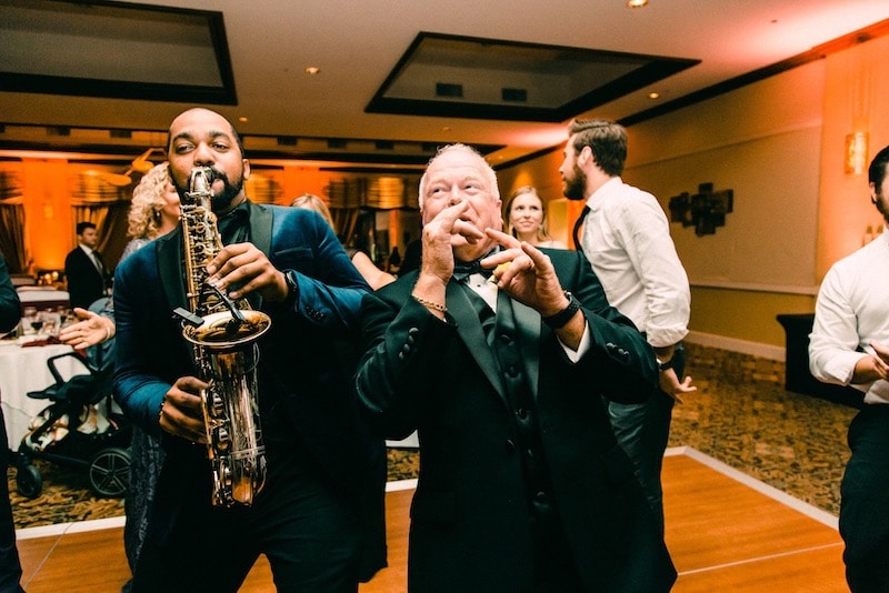 saxophone player performing on dance floor at wedding while father of the bride pretends to play an air trumpet standing next to him