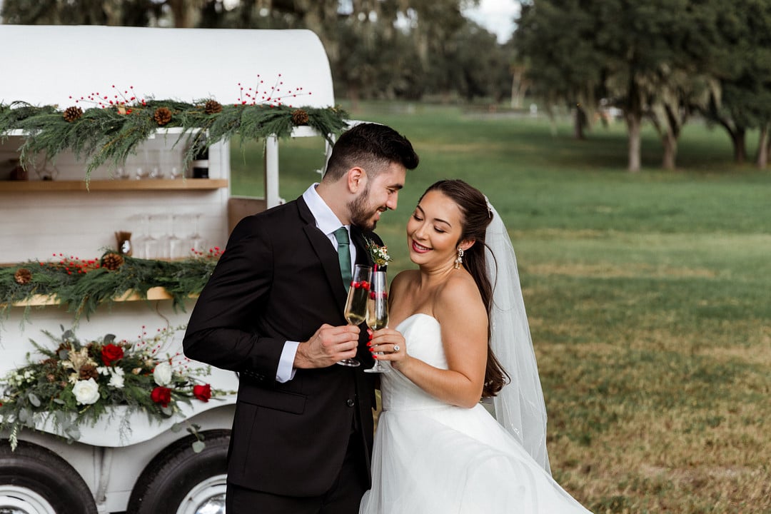 groom looks at bride while both stand outside at wedding venue with champagne in hands