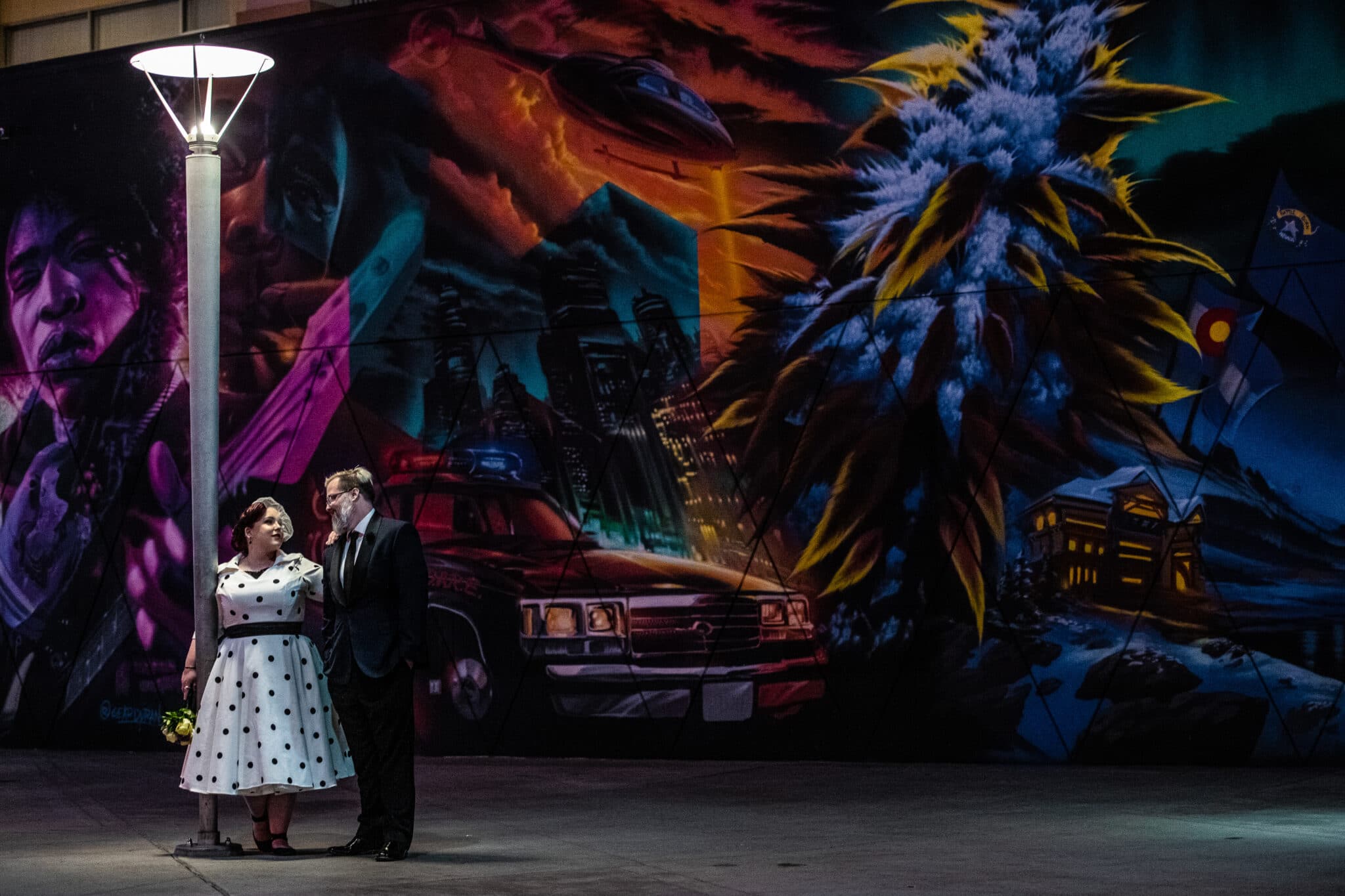 bride and groom standing in front of mural at night