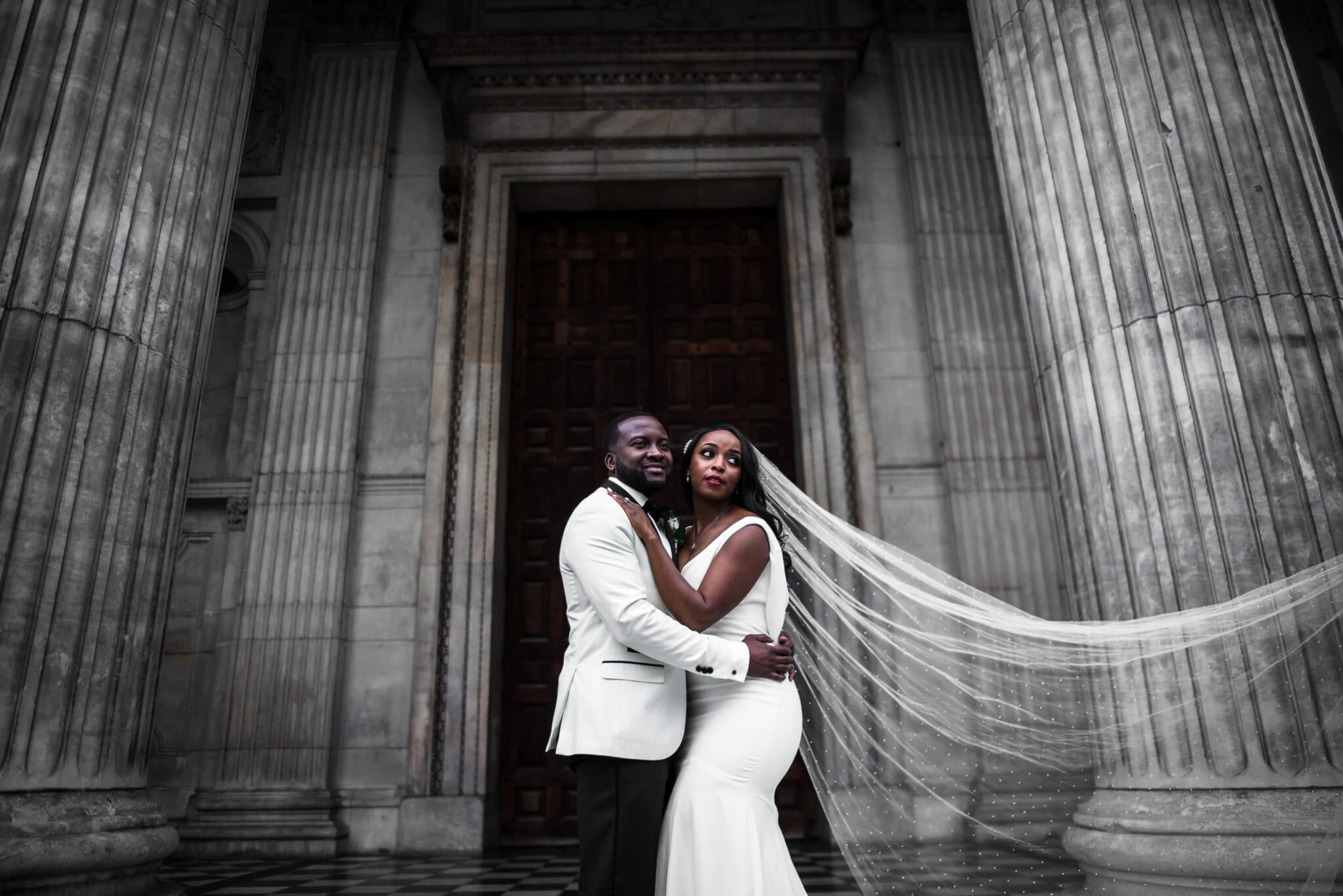 groom and bride with veil blowing outside columns