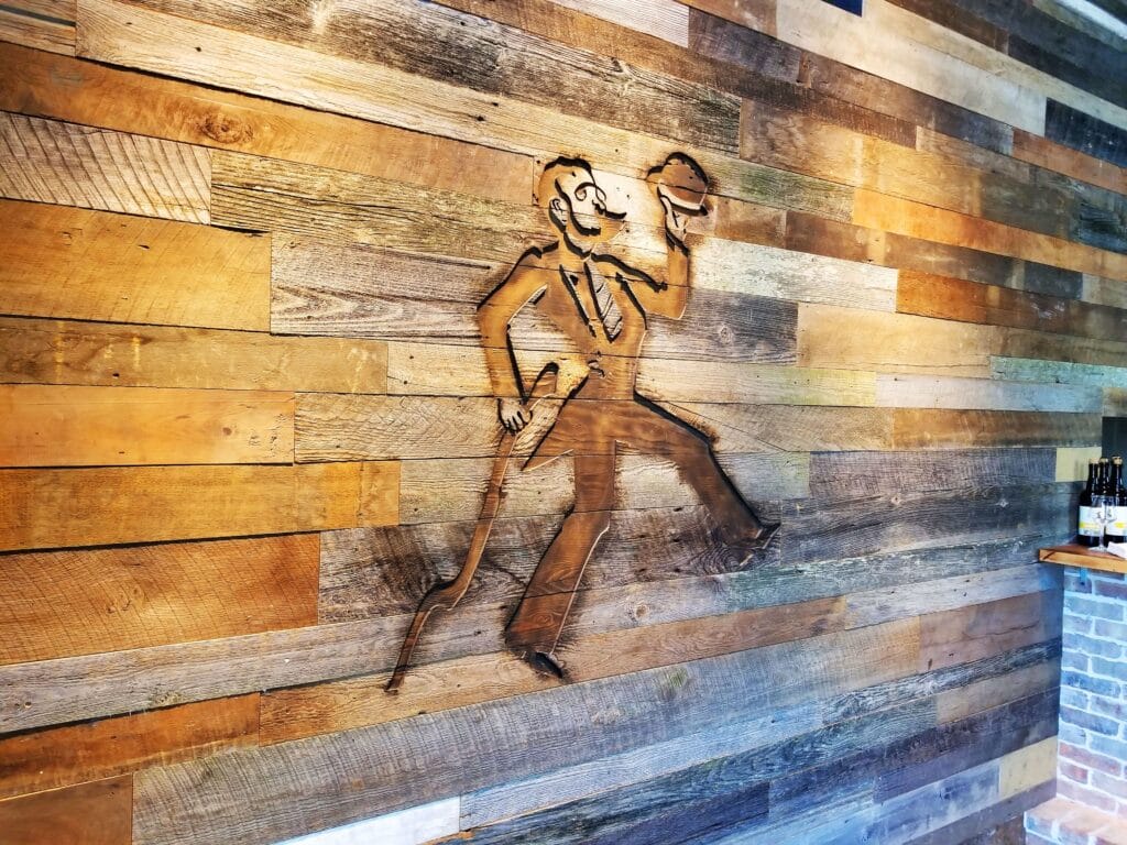 wood panel wall with engraved image of man in suit with hat and cane - logo for crooked can brewing company in winter garden florida