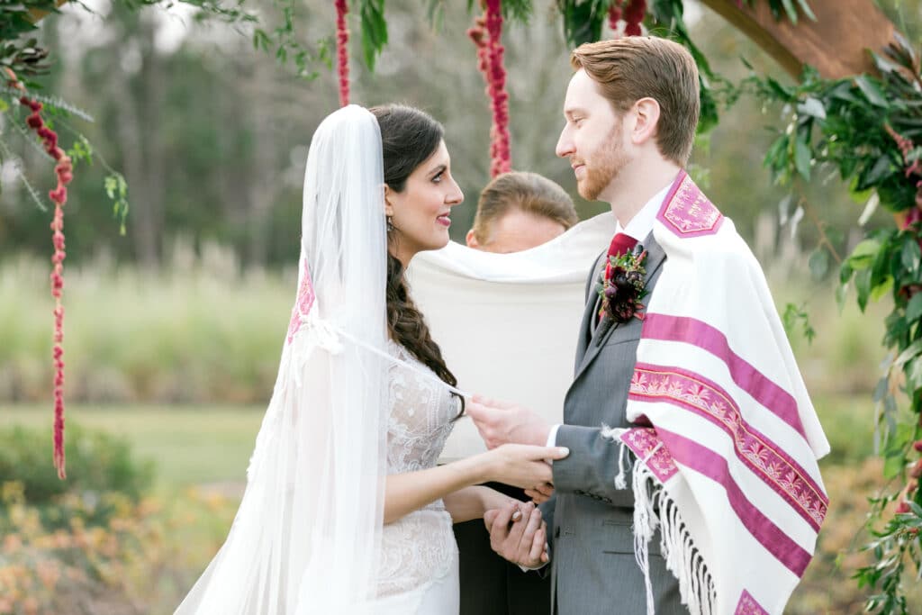 bride and groom embracing during wedding ceremony taking place outside under a vine covered arch