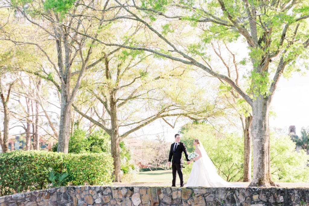 bride and groom walking along top of stone wall underneath large trees