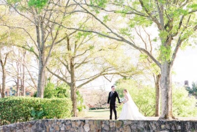 bride and groom walking along top of stone wall underneath large trees