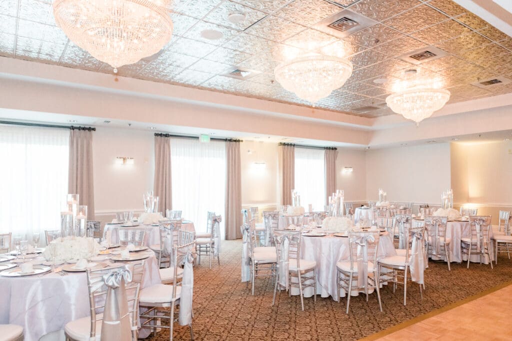 indoor ballroom setup for wedding reception, with multiple chandeliers, at least 6 tables all fully decorated
