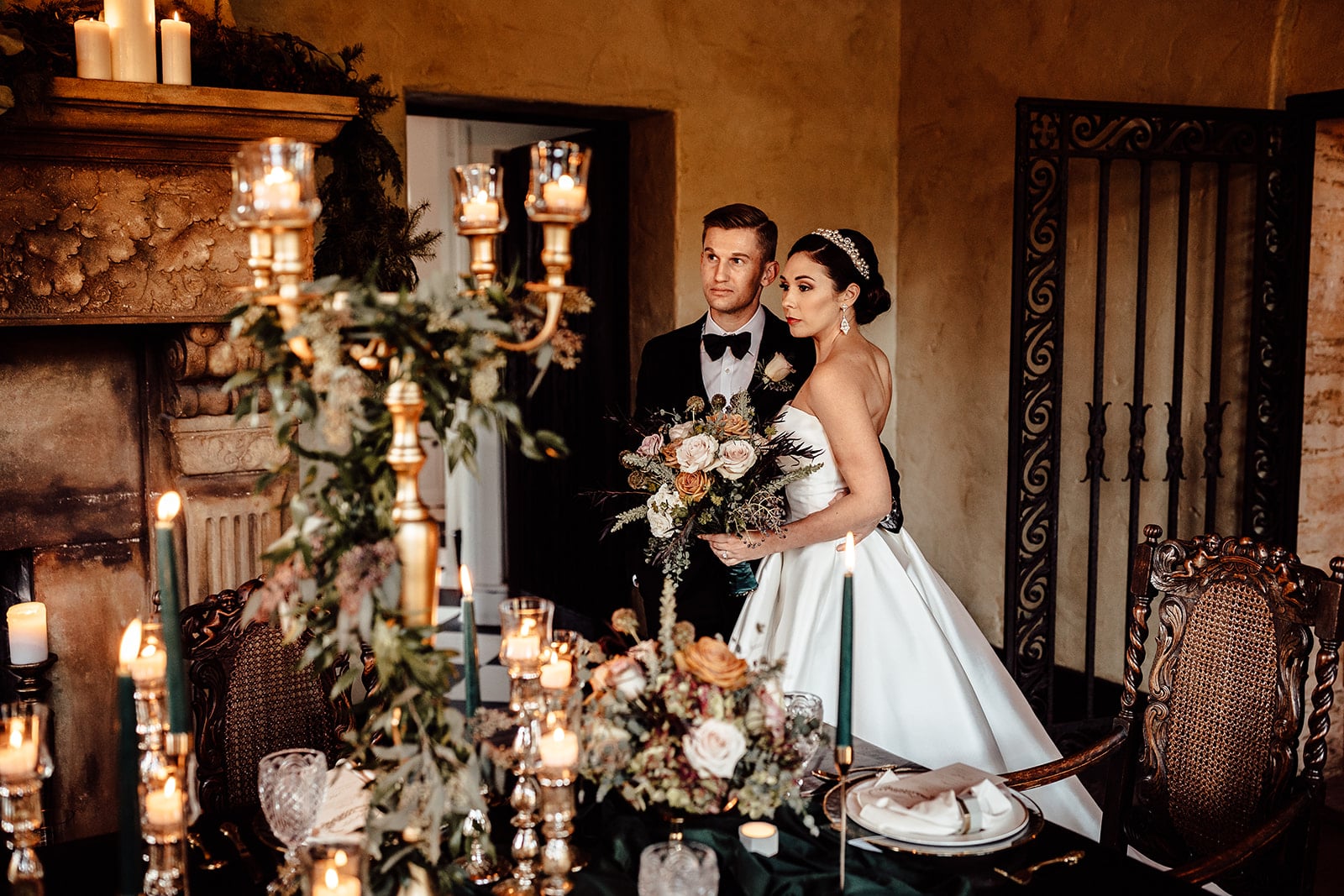couple on wedding day stand close to each other looking off in the distance to the left in front of decorated table with candelabra and greenery