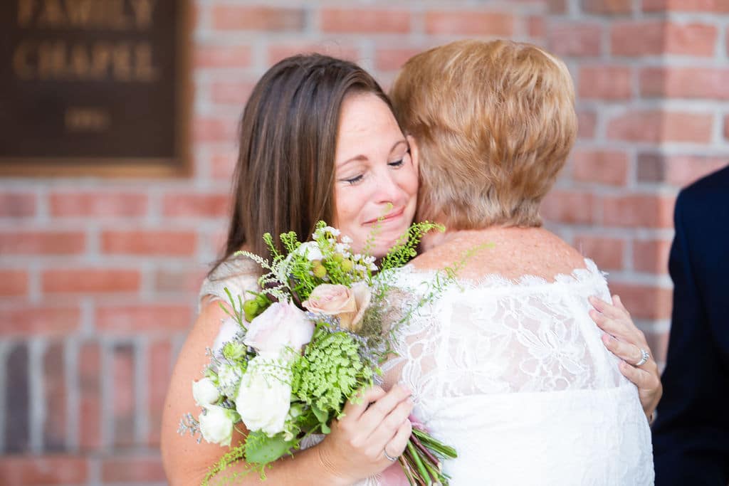 bride hugging matron of honor holding bouquet outside of wedding chapel