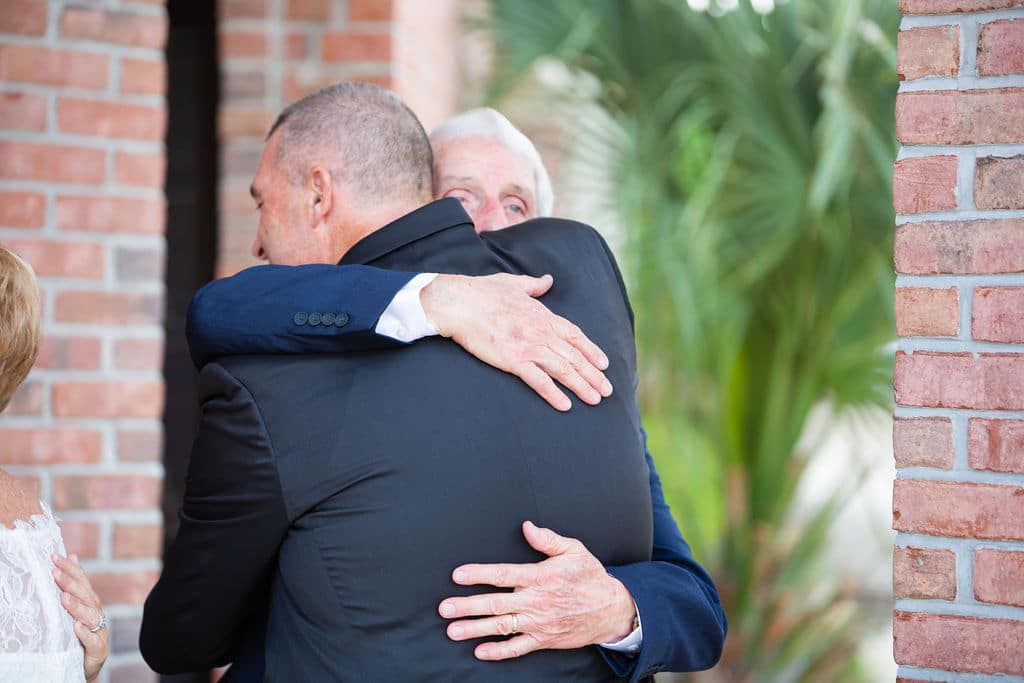 groom hugging man of honor outside near brick columns of wedding venue
