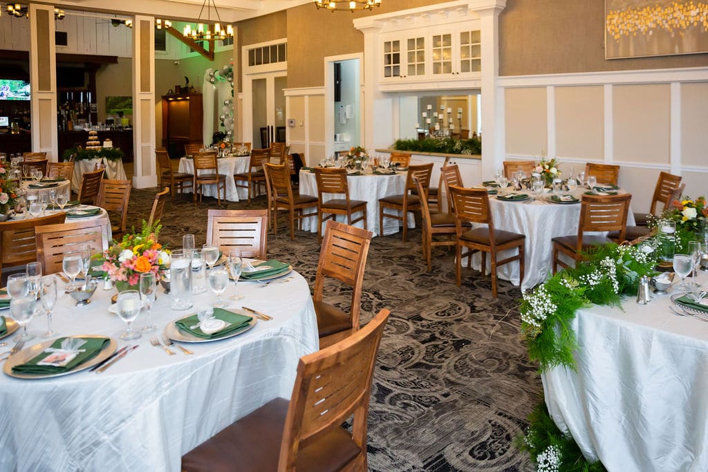 empty wedding reception space with wooden chairs and round banquet tables set with white linen and green napkins on plates
