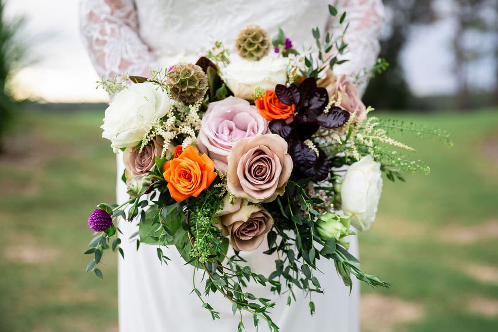close up of brides bouquet with rose light pink and orange colored flowers while bride holds it in front of her