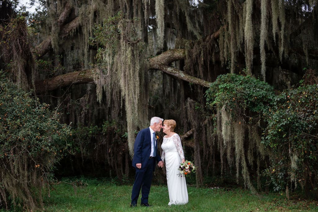 couple lean in to kiss in front of big cypress trees for wedding portraits