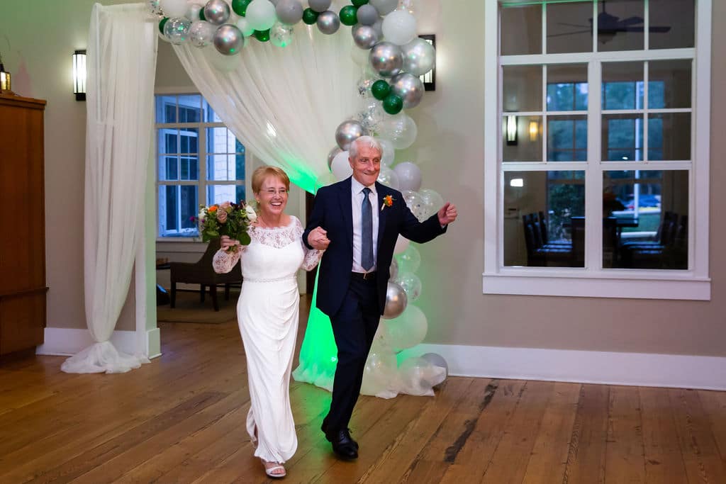 grand entrance of bride and groom into wedding reception through doorway with drapery and half balloon arch with silver white and green balloons