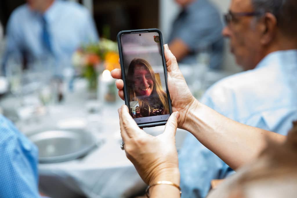guest at wedding holds phone on facetime with a woman while at wedding reception