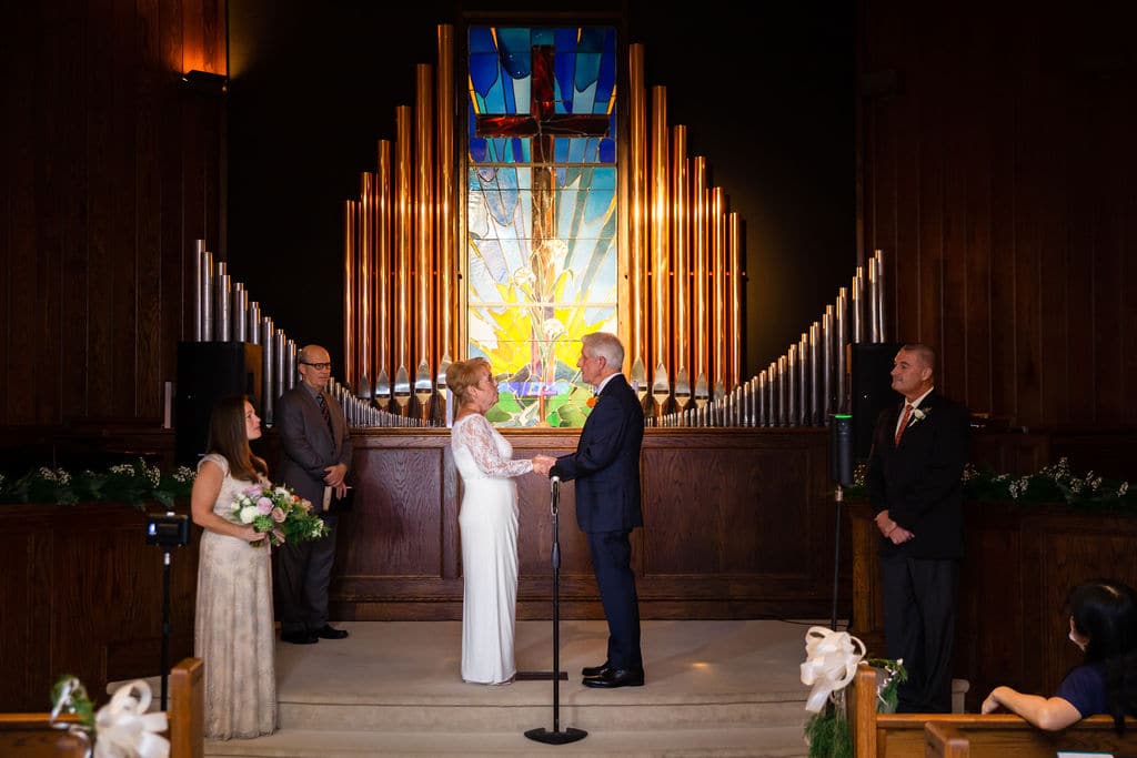 couple holds hands in the front of the chapel in front of stained glass window about to be married