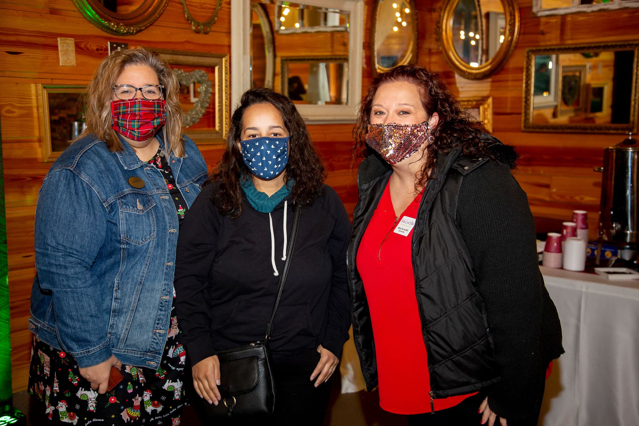 three woman stand next to each other wearing masks for picture at holiday party