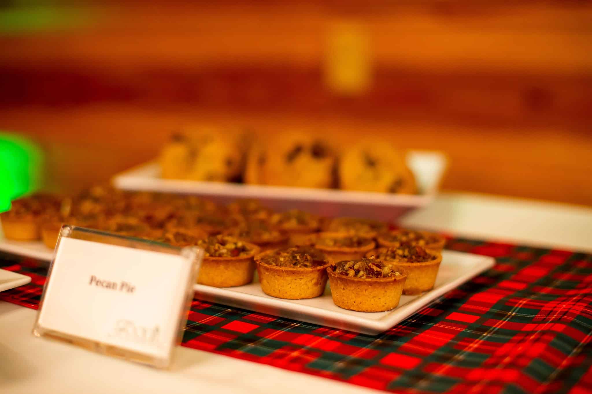 plate of mini pecan pies in front of plate of cookies on plaid green and red linen with sign for pecan pies in front