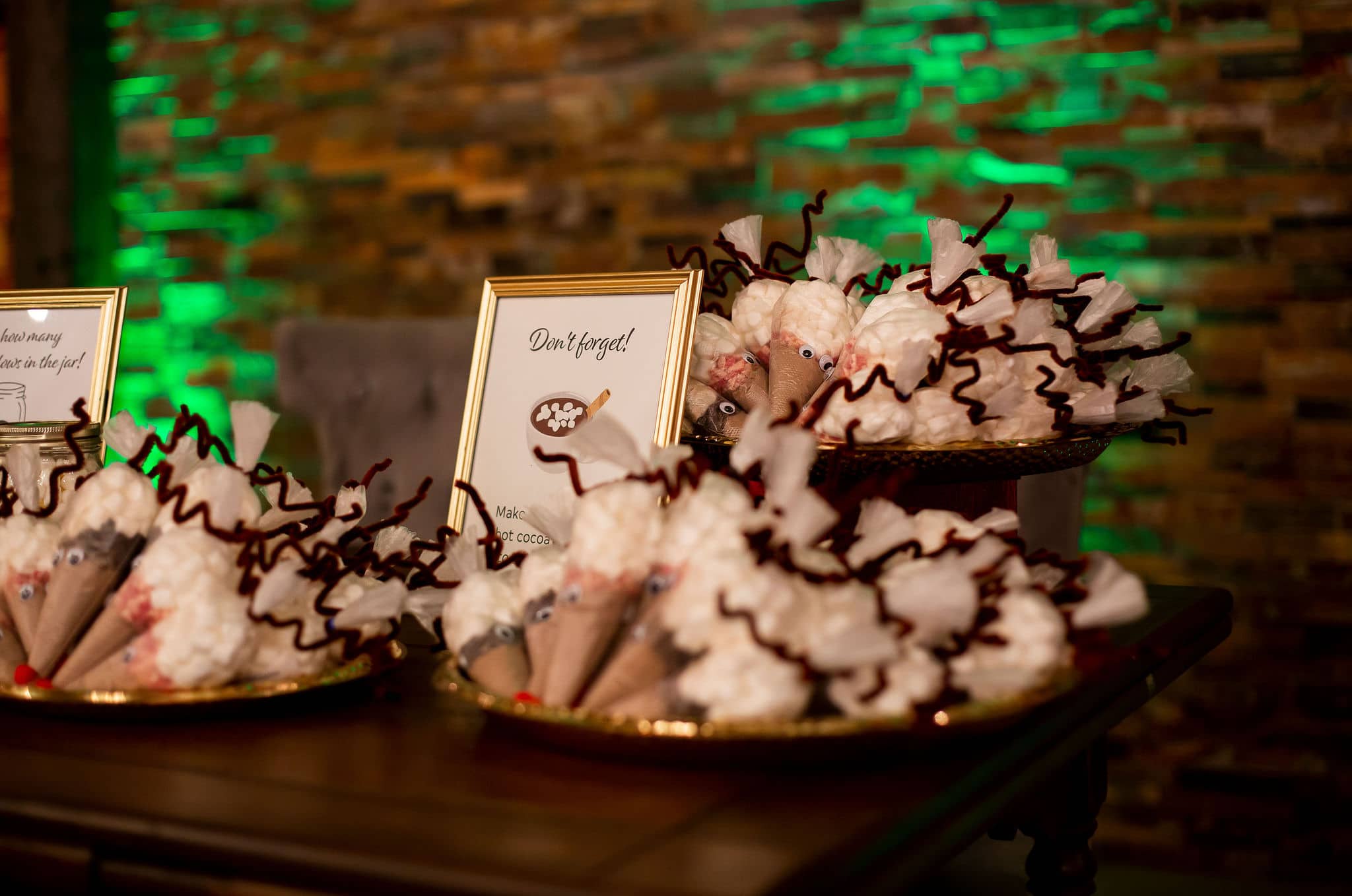 cones filled with hot cocoa powder and toppings of chocolate chips and candy canes on three different platters with sign next to it and green uplighting behind