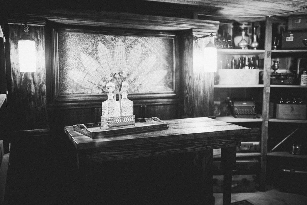 black and white picture of room with stained glass window and bottles on shelves as well as decorative bottles on high top table