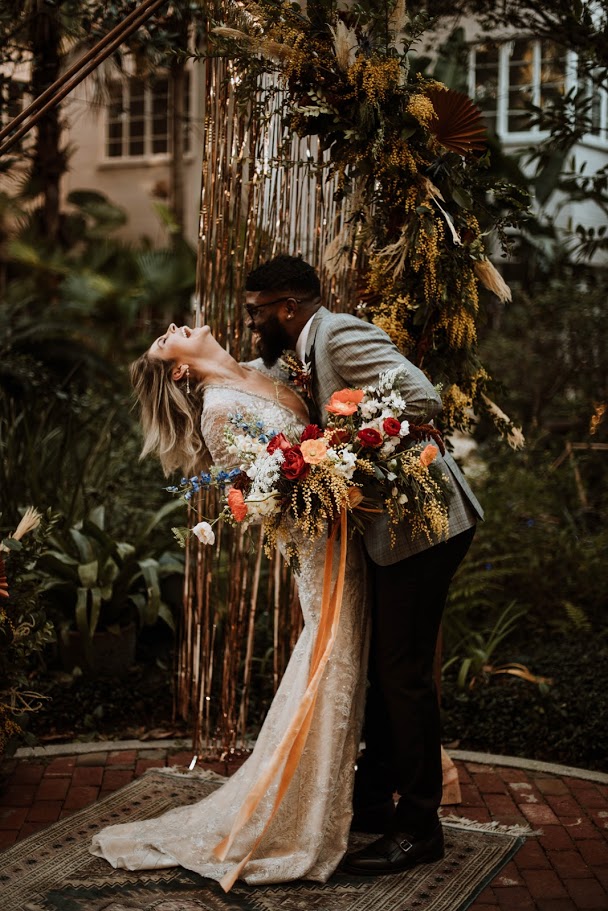 bride and groom embracing and laughing while holding large boho wedding bouquet