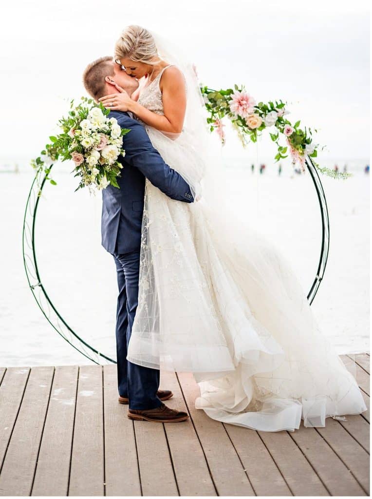 groom lifting bride, kissing in front of ring with flowers