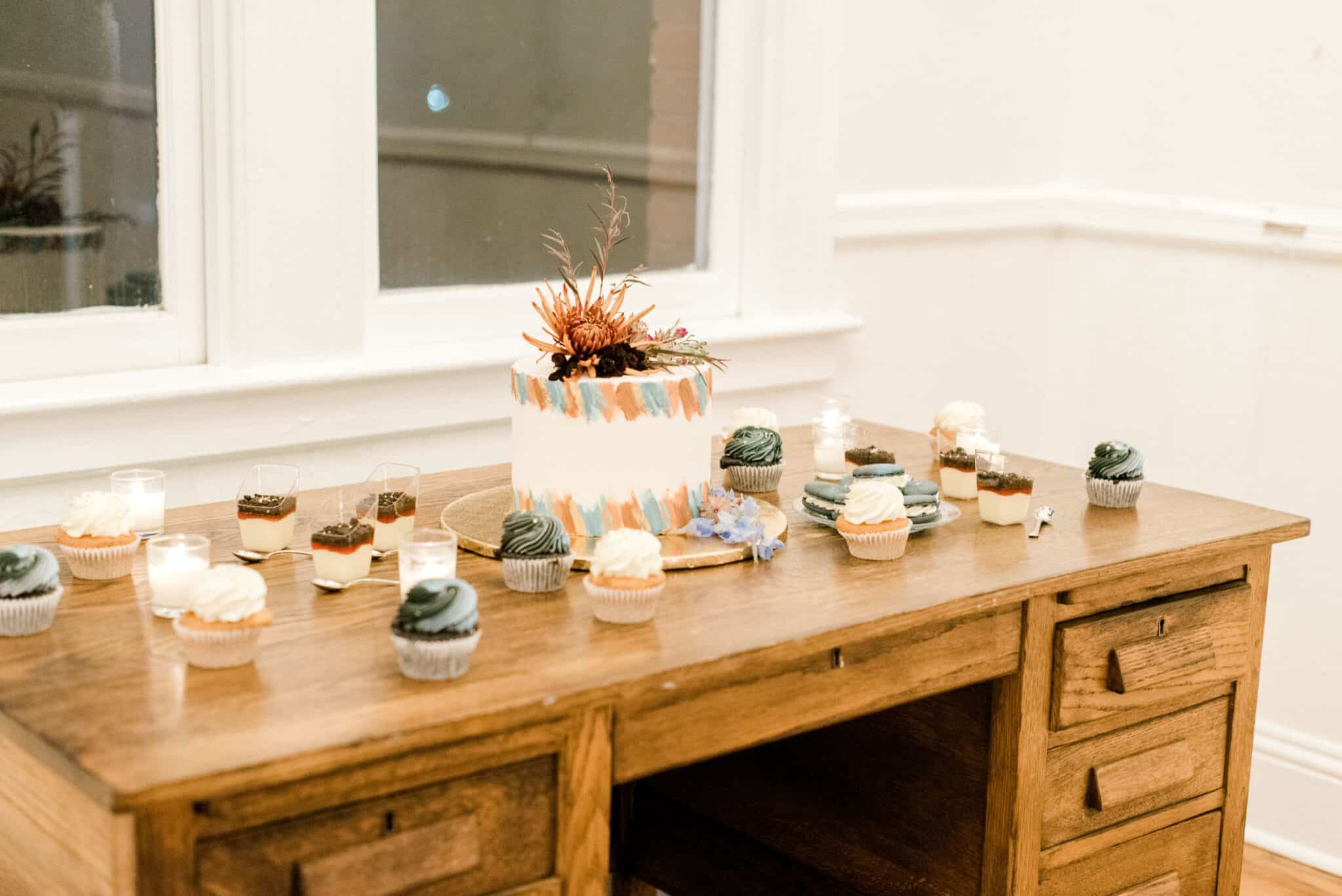 dessert selection on top of old wooden desk at wedding including cupcakes and unique one layer wedding cake