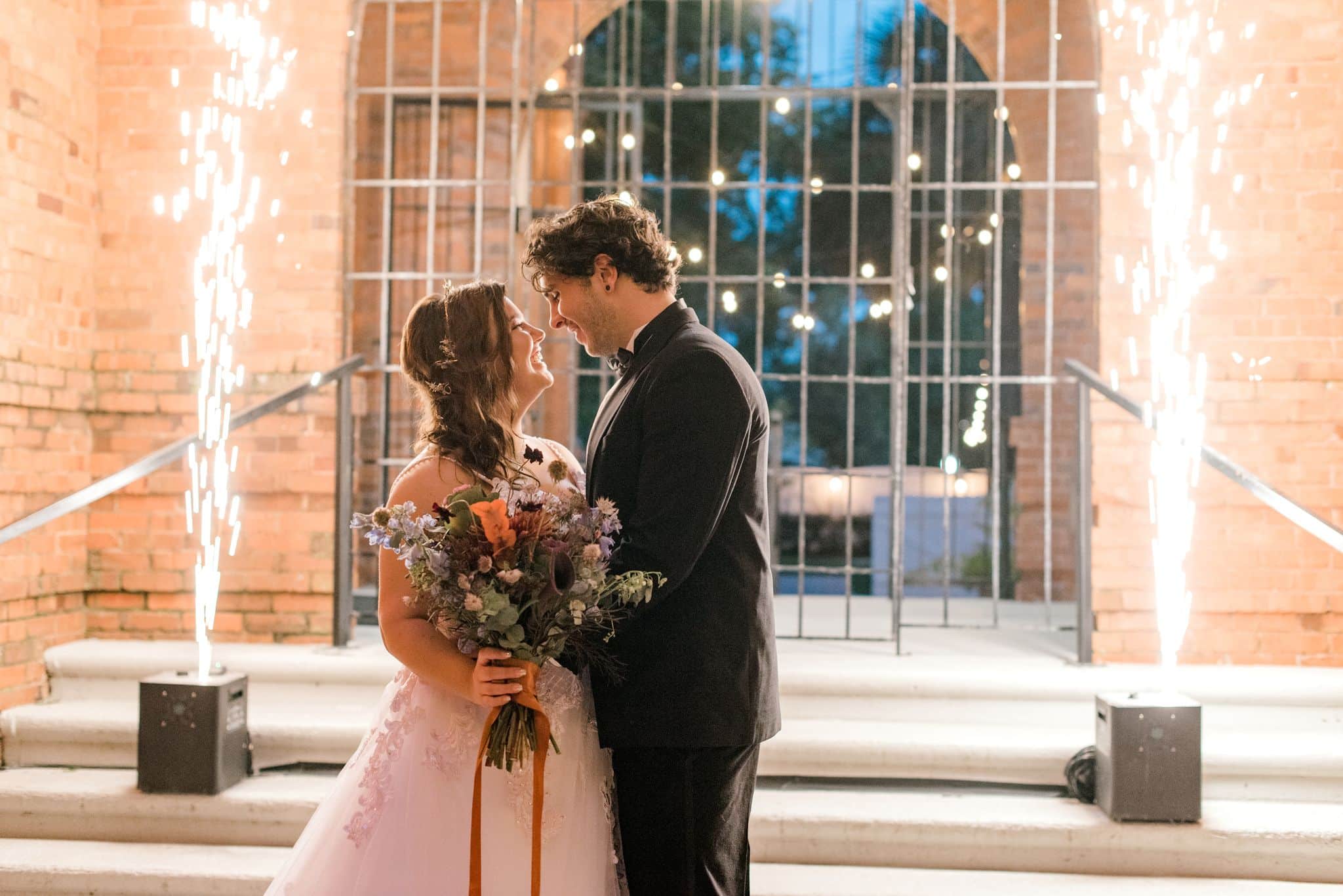 bride and groom look at each other in front of signature photo spot at central florida wedding venue with two sparkler machines on either side of them