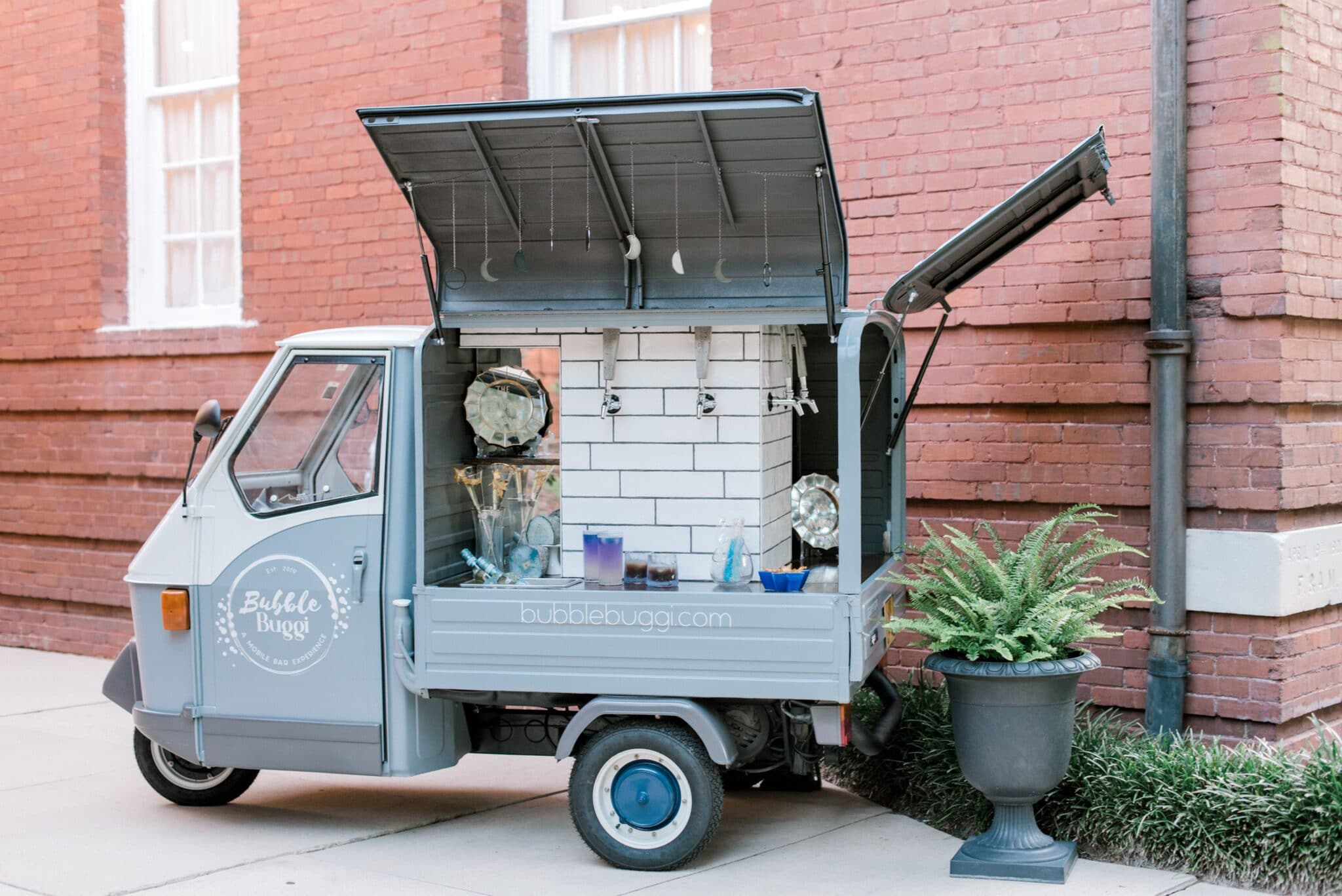mobile bar cart with signature cocktail on it and doors open to reveal drink taps outside wedding venue