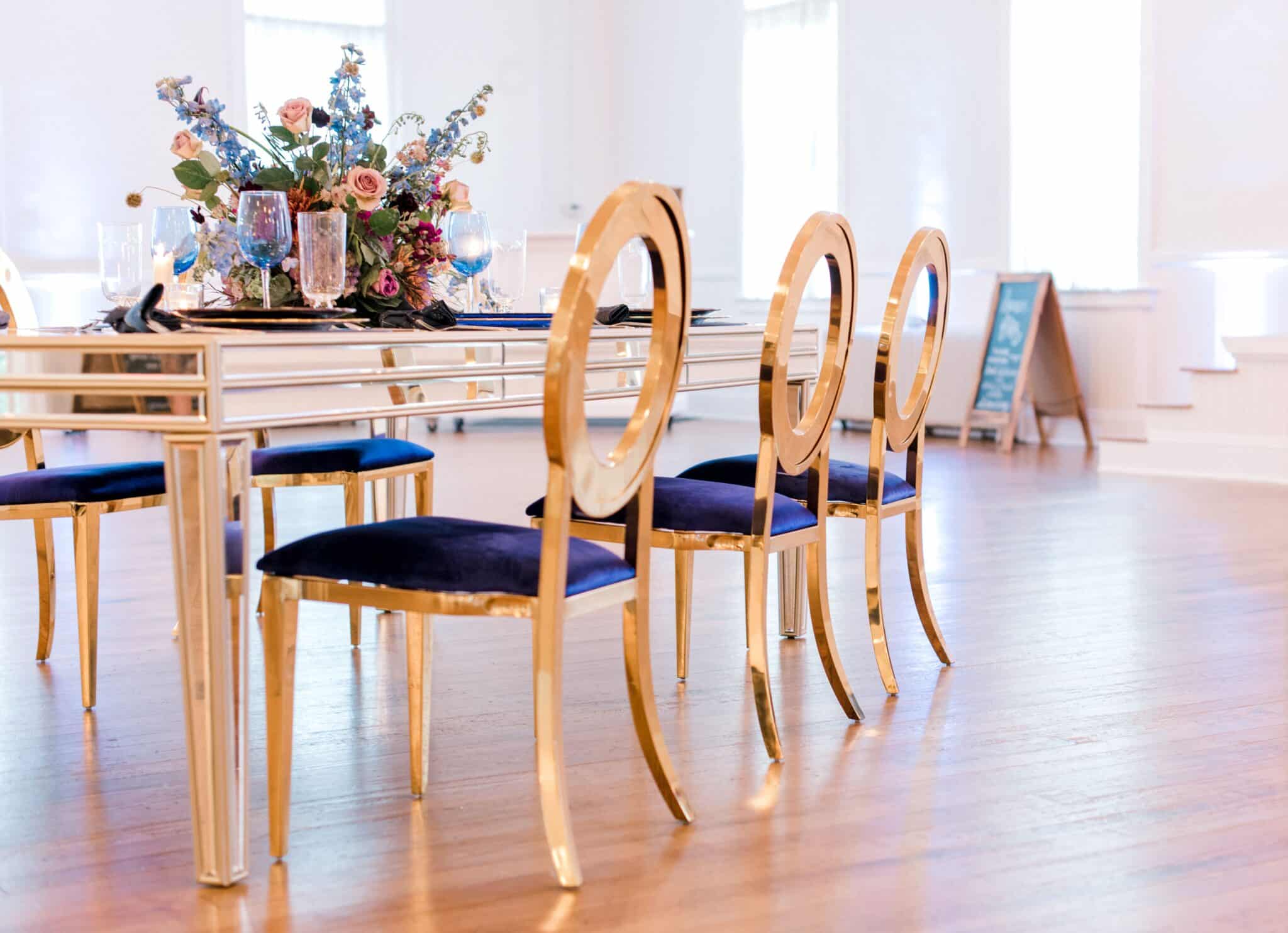 golden chair with blue padded eat and golden table with decor for a wedding styled shoot on top with hard wood floors