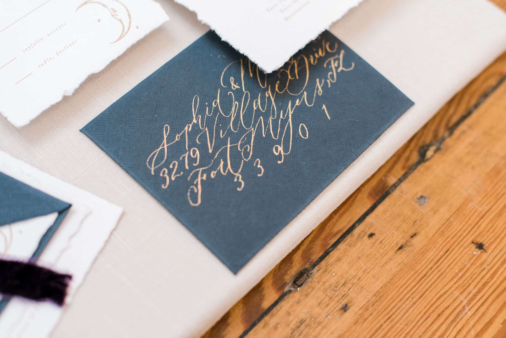 close up of outside envelope for wedding invitation with gold lettering and navy blue envelope