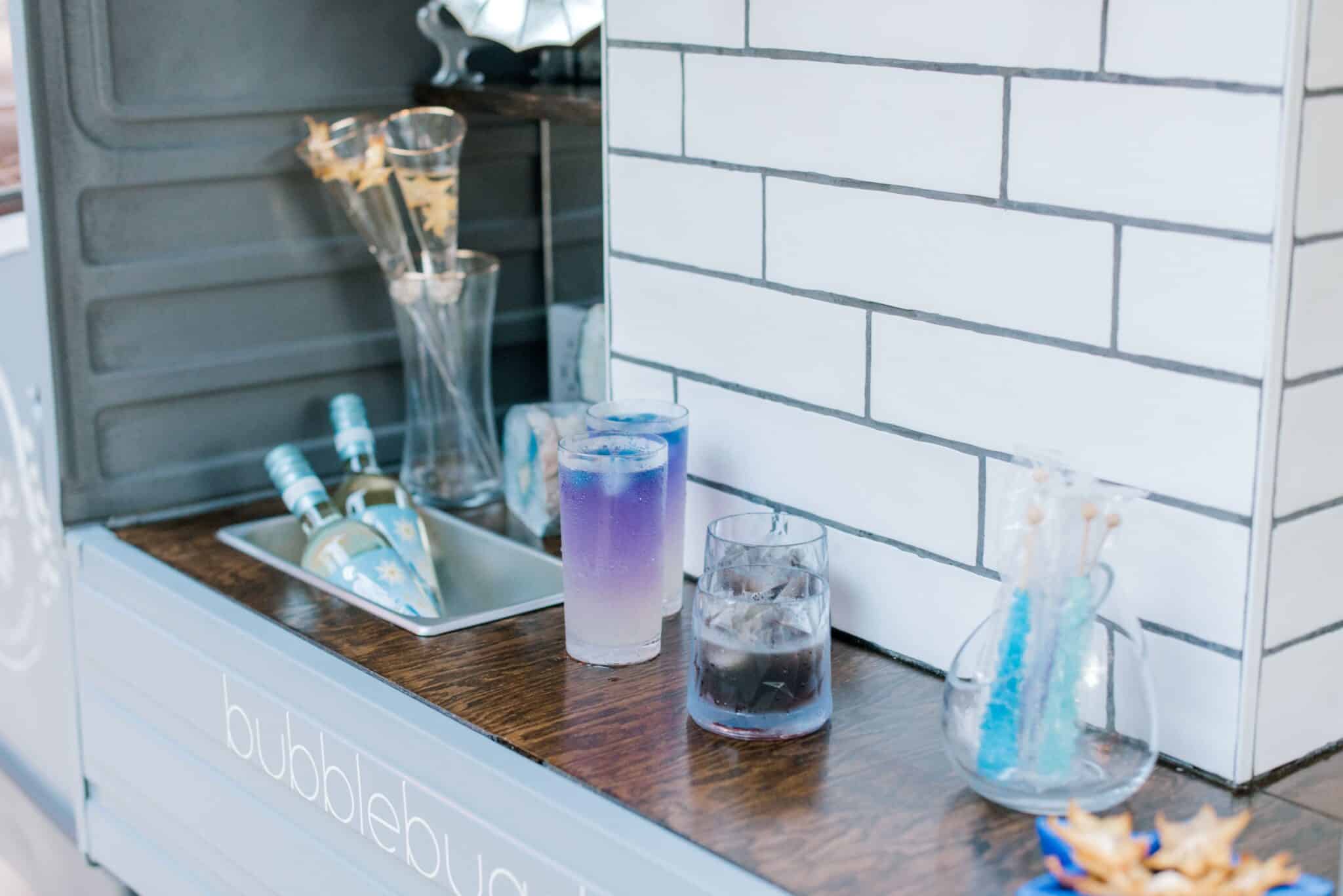 close up of mobile bar cart featuring signature drinks that are unique and purple along with chilled bottles of wine
