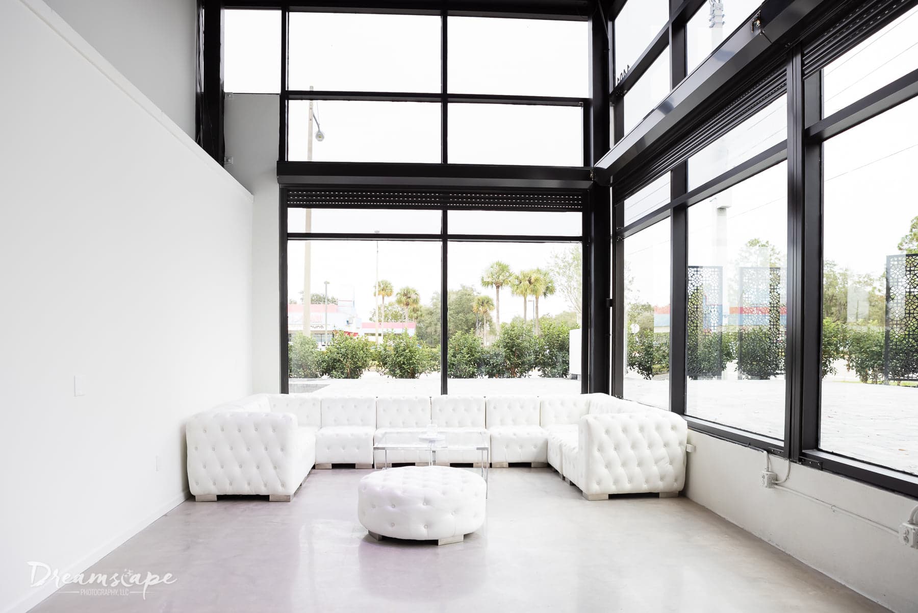 small area with white wall to the left and the other two sides are big windows from floor to ceiling with white leather sofas in the space 