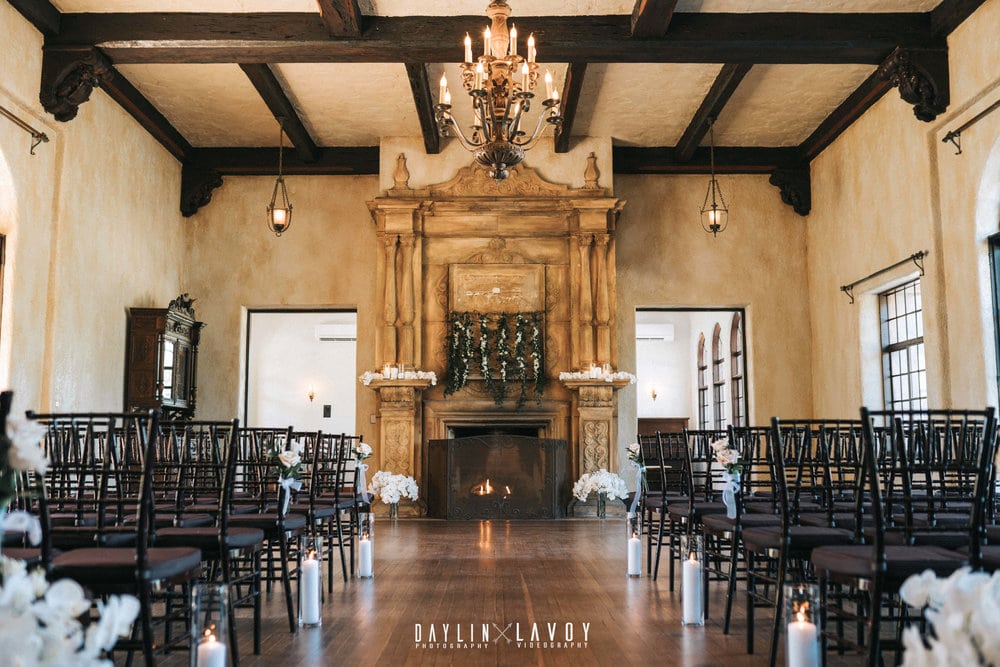ceremony set up inside with floor to ceiling fire place and decorative mantle in the front with floral arrangements in the front and candles down the aisle with mahogany chiavari chairs